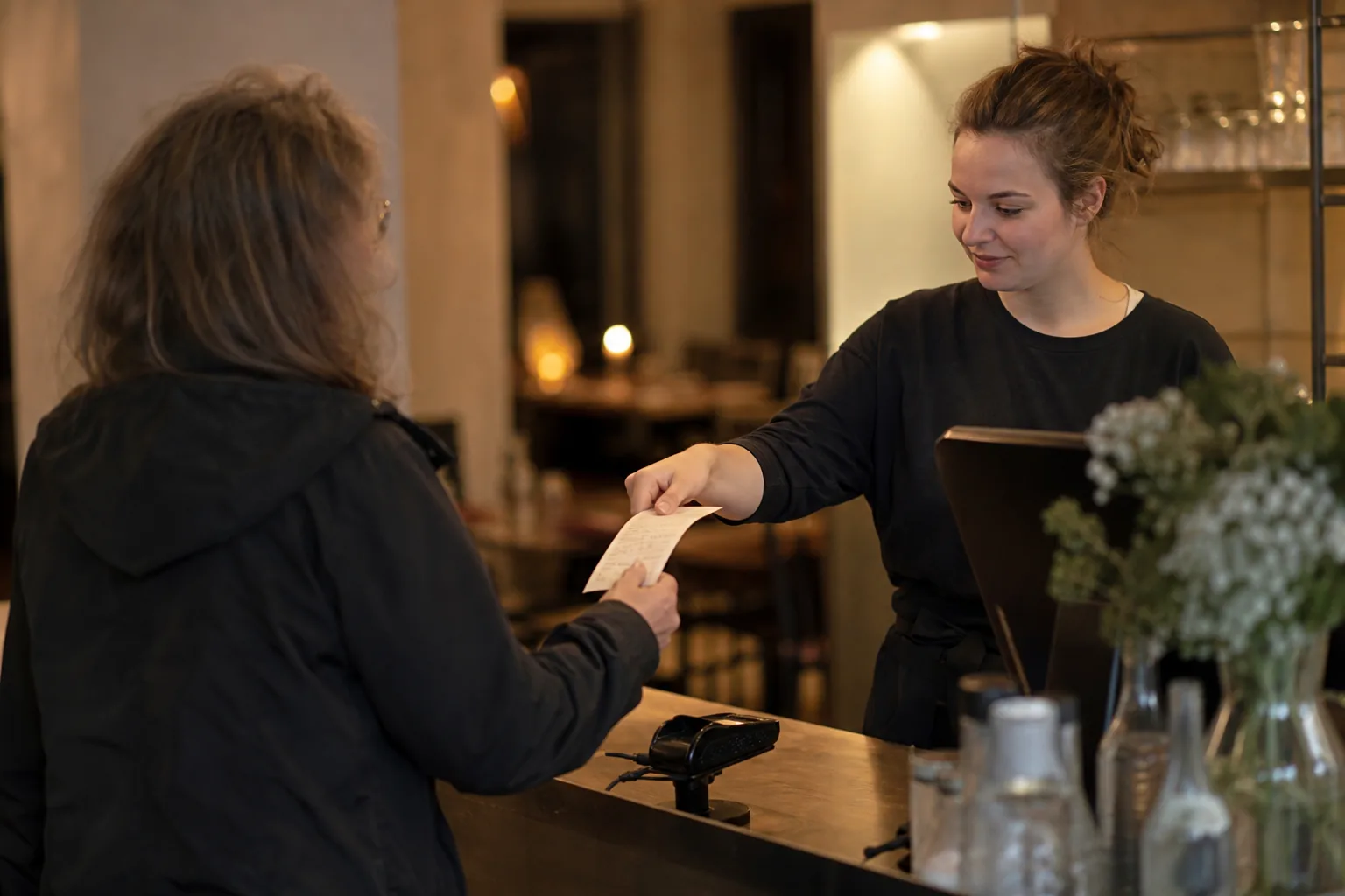 Servicekraft gibt einem Gast an der Restaurantkasse einen Kassenbon.