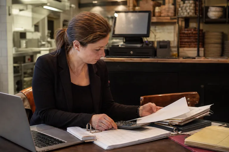 Restaurantleiterin bereitet am Laptop die Kassenmeldung mit Unterlagen vor.