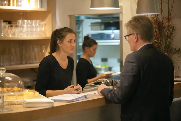 Caféleiterin organisiert an der Theke Unterlagen für einen Besucher.