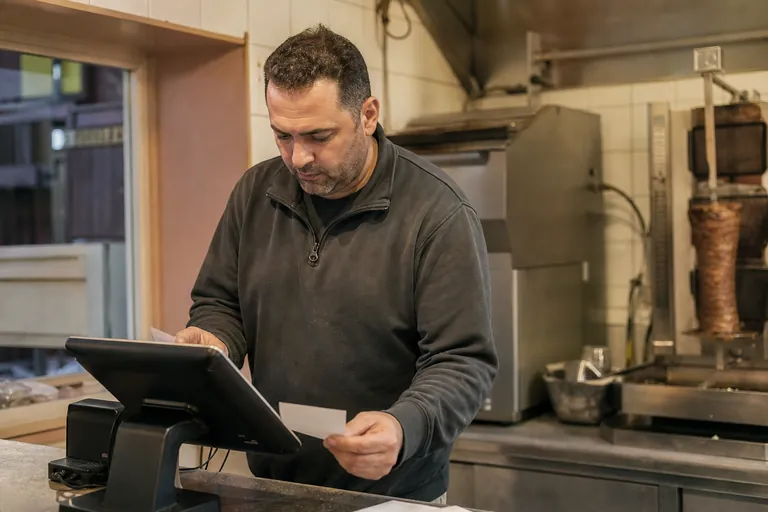 Imbissbetreiber prüft eine TSE-Seriennummer anhand von Kassenunterlagen.