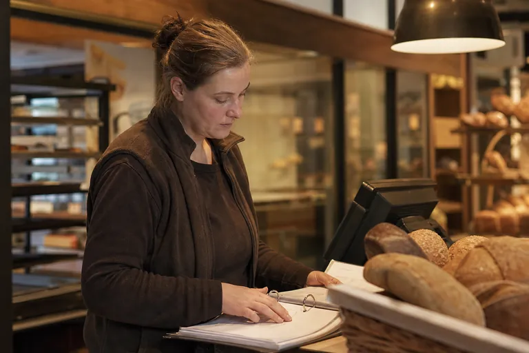 Bäckereifilialleiterin prüft Kassenunterlagen neben einer Verkaufskasse.